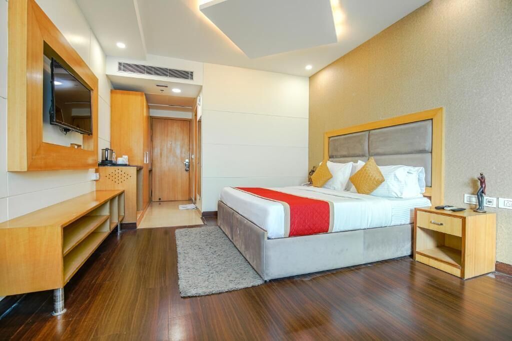 A modern hotel room with a large bed, a TV mounted on the wall, a wooden nightstand, and a desk with a chair.