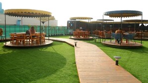 Eine Dachterrasse mit Holztischen und -stühlen unter Markisen, umgeben von grünem Kunstgrün.