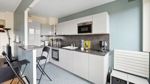 A modern kitchen with white cabinets, a built-in microwave, and a grey countertop. - Appartement Akena - Welkeys (Boulogne-Billancourt)