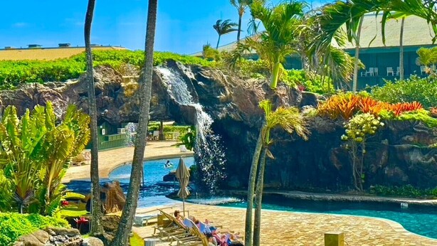 A pool area with a waterfall, lounge chairs, and tropical plants. - Lagoon View Resort Retreat (Lihue)