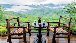Une terrasse en bois avec deux chaises et une table, d’où l’on peut admirer une vallée verdoyante et des montagnes.