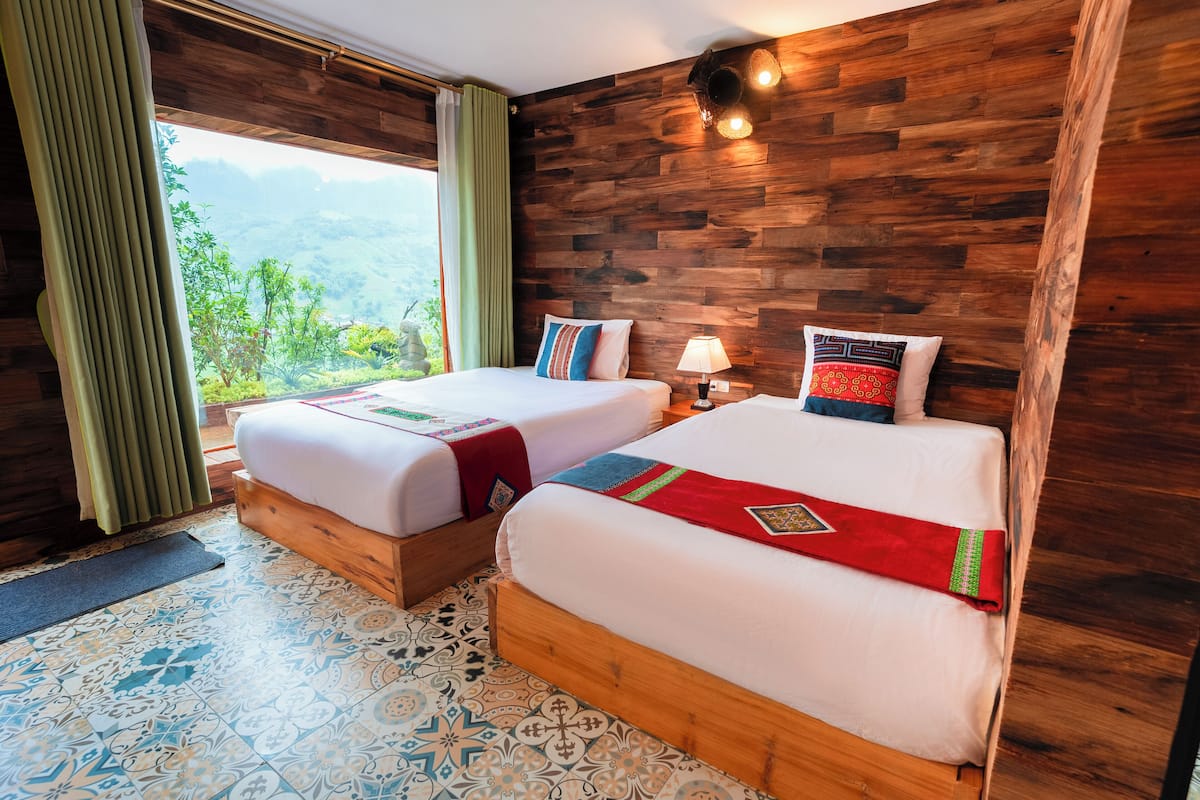Ein Hotelzimmer mit zwei Betten, einem Holzkopfteil, Blick auf Grünflächen und Mustertrennkies.