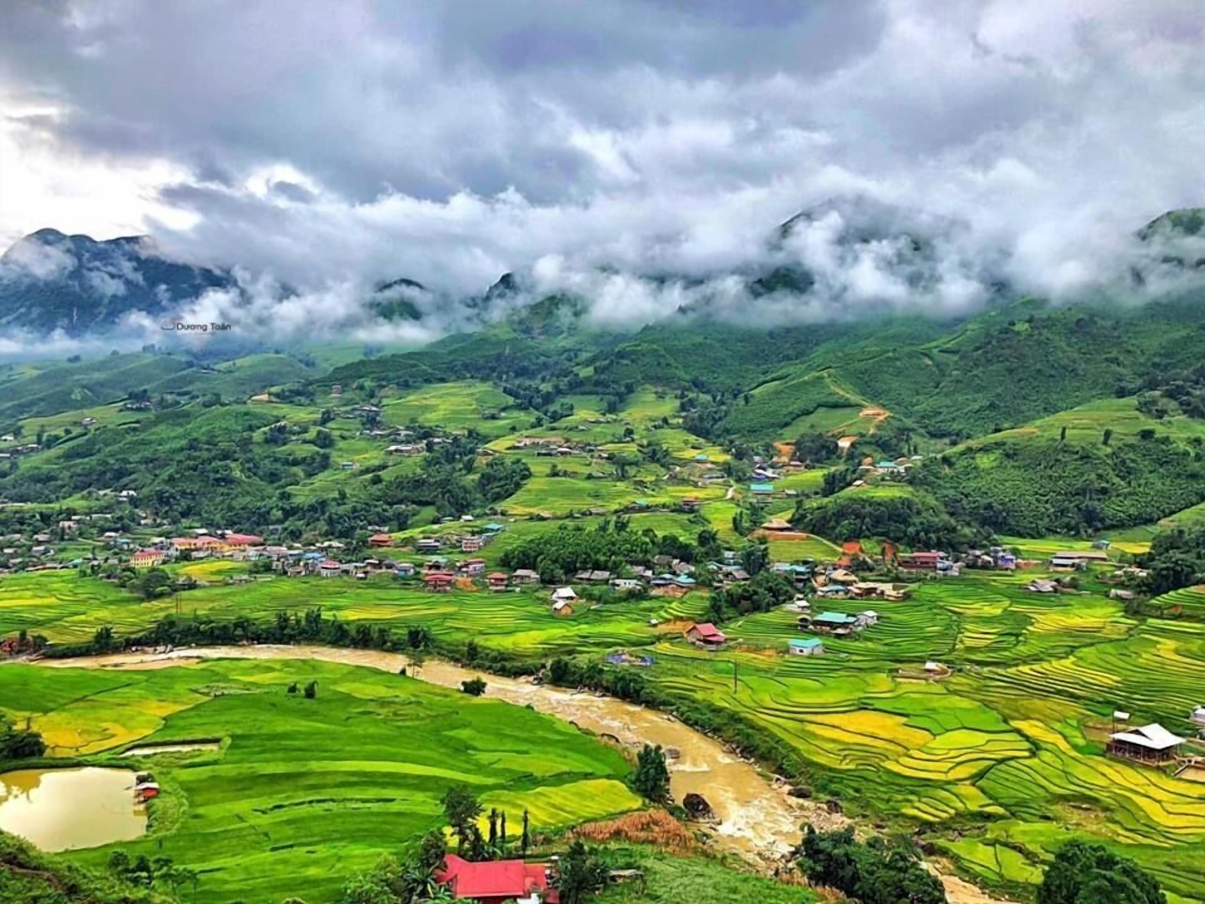 Une vue panoramique d’une vallée verdoyante, avec des champs en terrasses, un petit plan d’eau et des maisons dispersées.