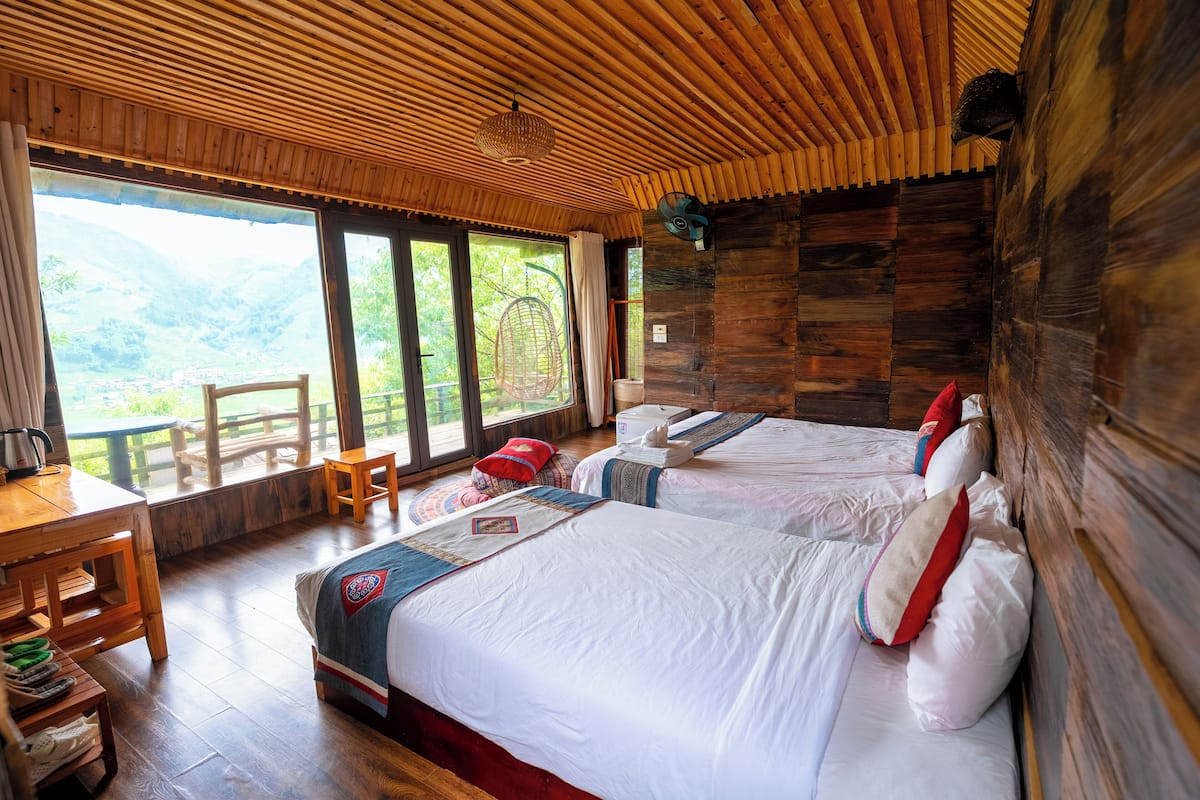 Ein Zimmer mit zwei Betten, Holzboden, einem Tisch mit Stühlen und großen Fenstern mit Blick auf eine Berglandschaft.