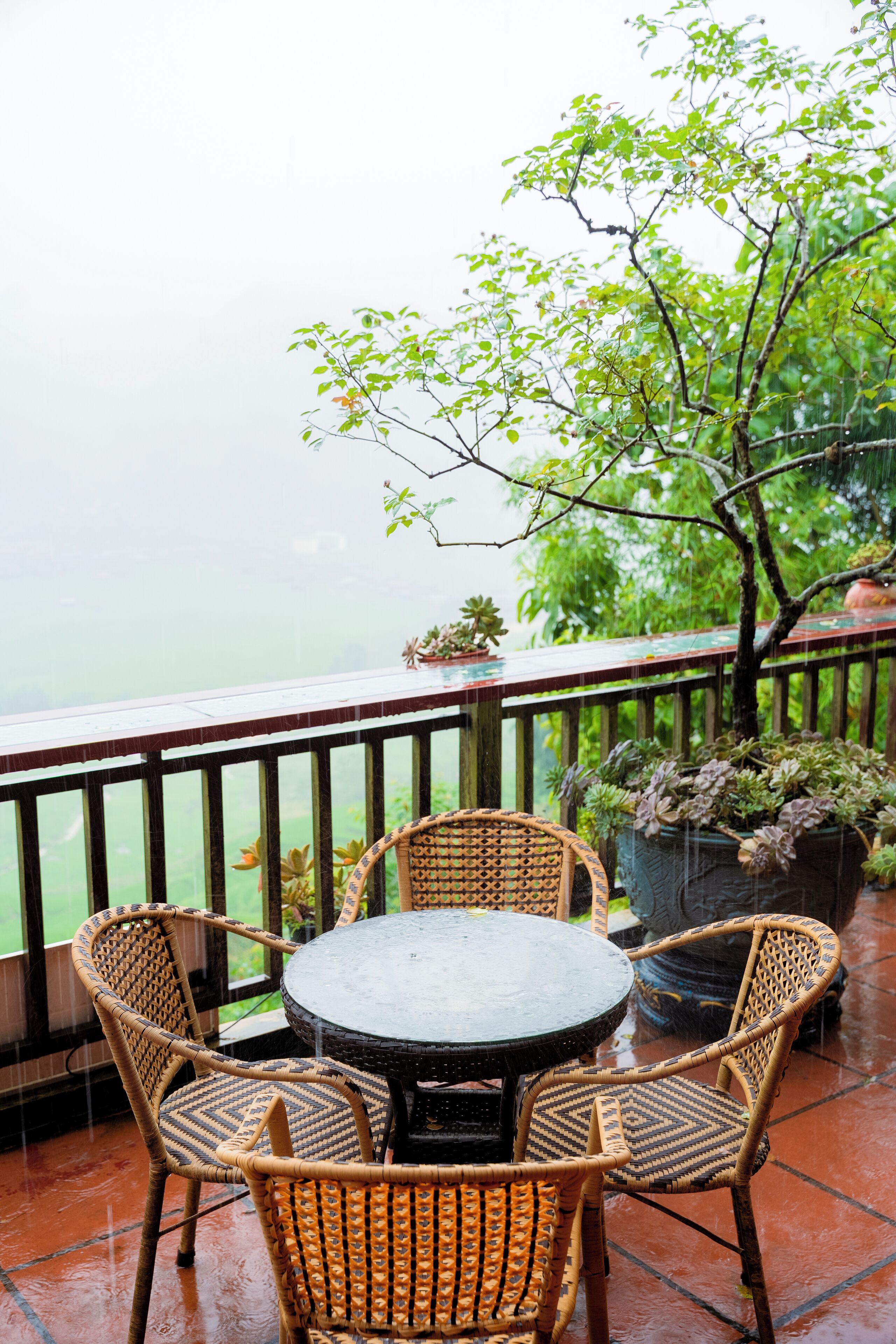 A covered outdoor seating area with wicker chairs and a round table, overlooking a body of water.