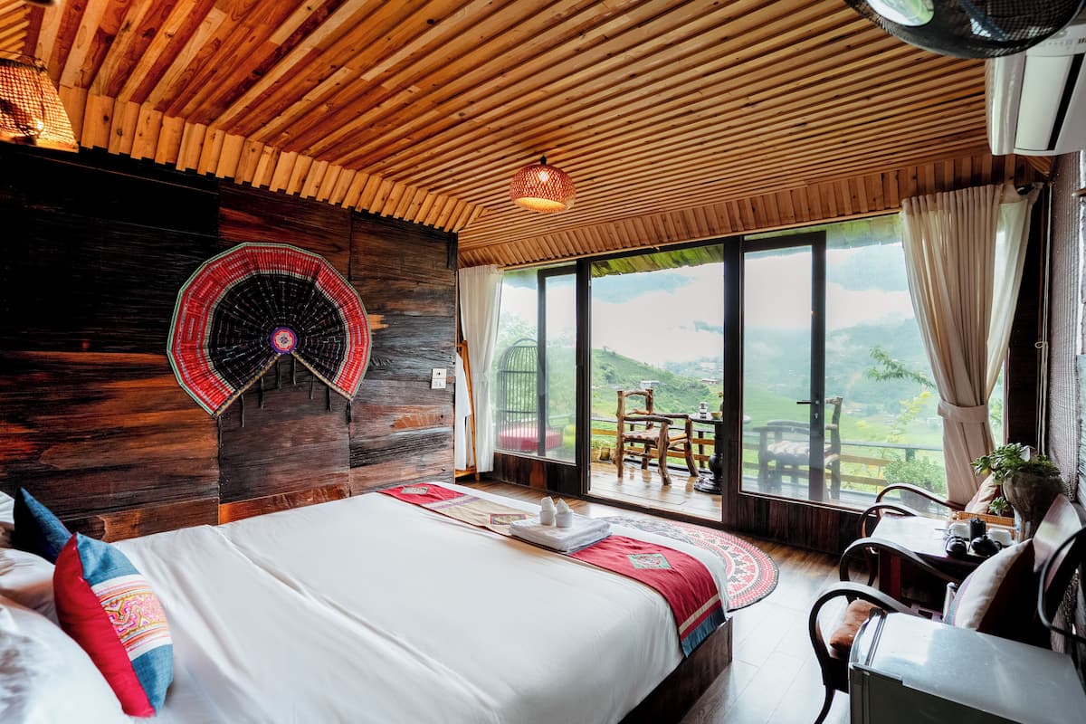 Ein Schlafzimmer mit einem großen Bett, Holzboden, Blick ins Freie und einem Essbereich mit Tisch und Stühlen.