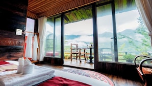 Une pièce dotée d’une grande fenêtre, d’un lit, d’un plafond en bois et offrant une vue sur les montagnes.