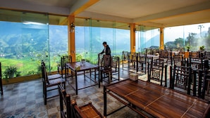 Un restaurant offrant une vue sur une vallée verdoyante, avec des meubles en bois et un serveur.