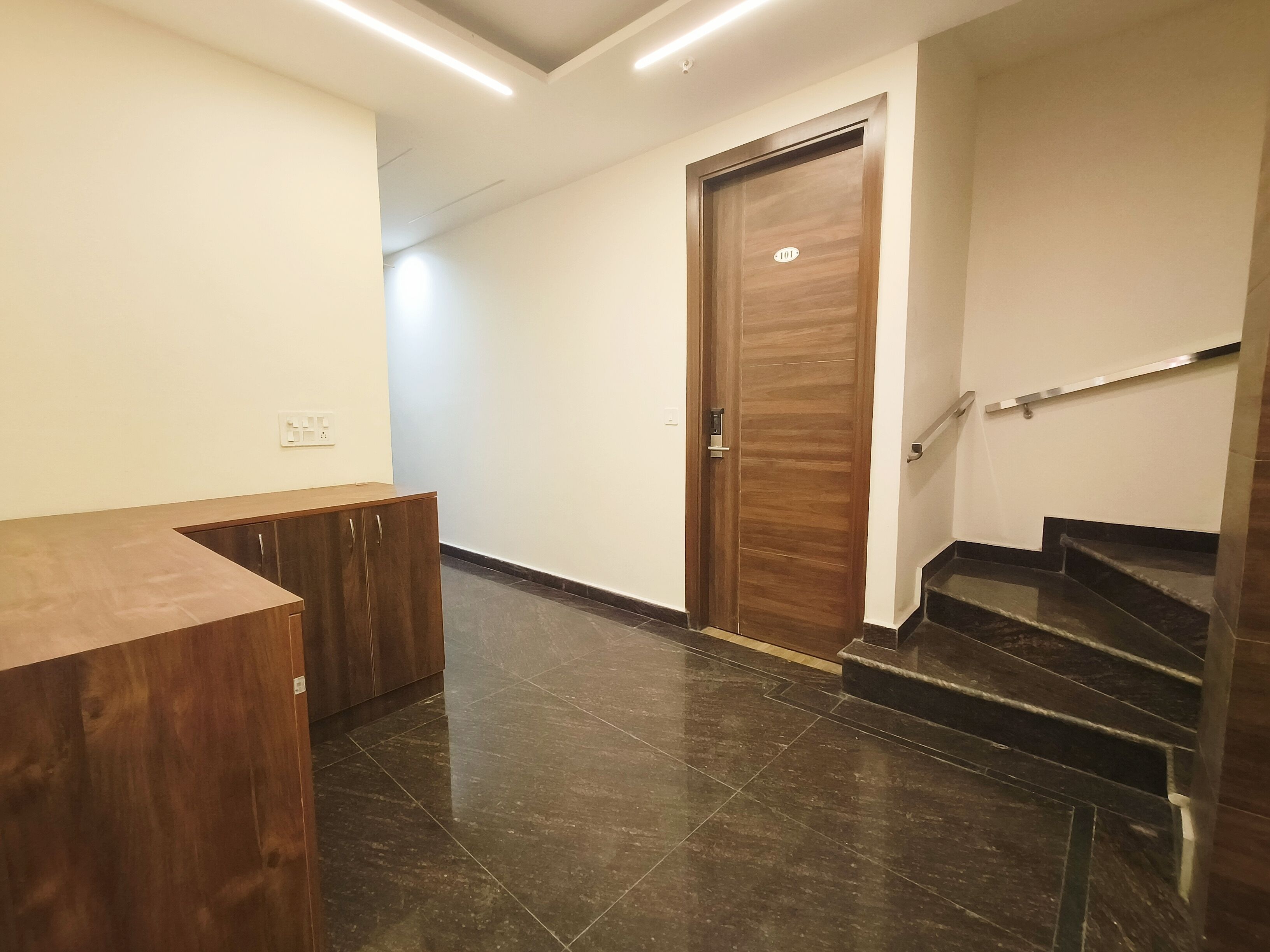 Un couloir avec un comptoir d’accueil en bois, une porte dotée d’une poignée et un escalier muni d’une main courante.