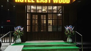 La entrada de HOTEL EAST WOOD, con una escalera alfombrada de color verde y dos jarrones de flores.