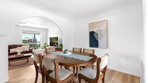 Un coin repas avec une table ronde en bois, six chaises et un grand tableau abstrait accroché au mur.