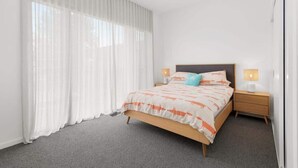 A bedroom with a bed, curtains, a nightstand, and a lamp.