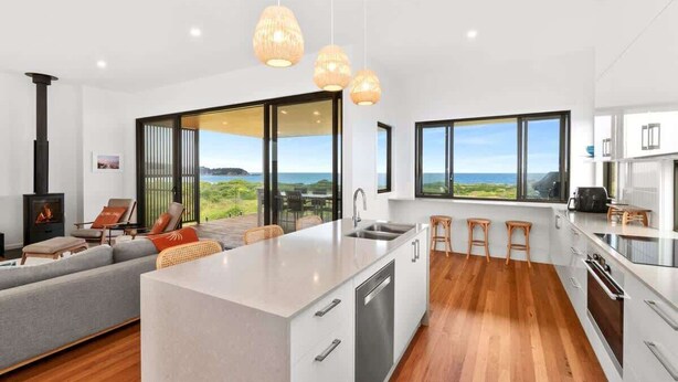 A modern kitchen with a central island, large windows, and a view of the outdoors.