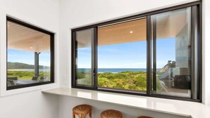 A room with large windows offering a view of a coastal landscape, a white wall, and two wicker chairs.