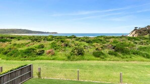 A grassy area with a wooden fence, a clear sky, and a distant view of the coastline.