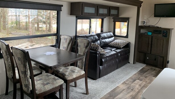 Een gezellig interieur van een camper, met een eettafel, stoelen, een bank en een aan de muur bevestigde televisie.