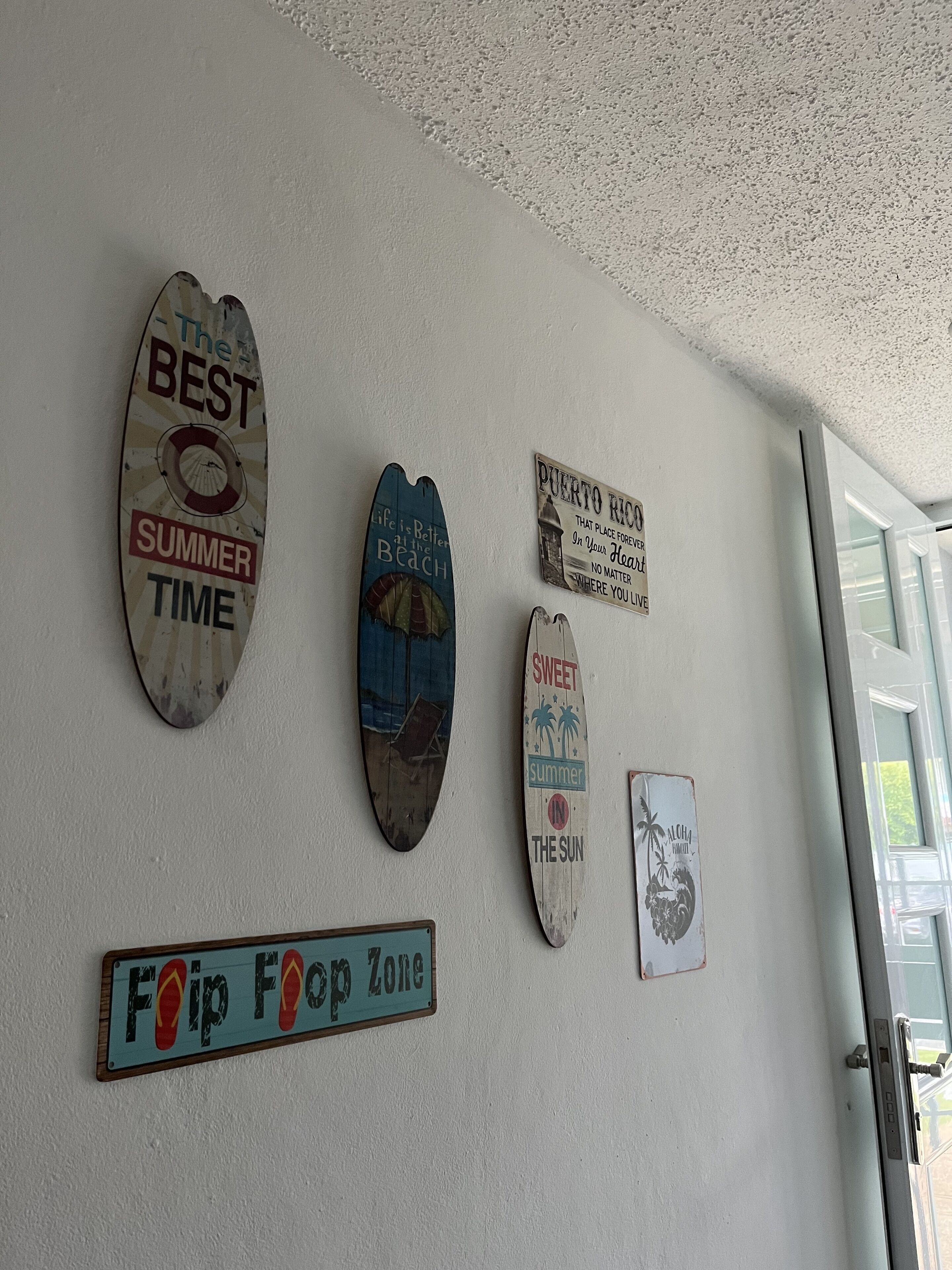 Eine Wand mit verschiedenen Schildern, darunter eines mit der Aufschrift 'The Best Summer Time' und ein weiteres mit 'Foop Foop Zone'.