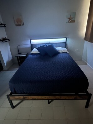A single bed with a headboard, a bedside table, and a wall-mounted shelf.