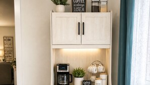 Une petite cuisine équipée d’une machine à café, avec un panneau indiquant : « Un café, c’est toujours une bonne idée », et une plante posée sur le dessus.