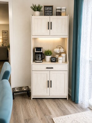 Una kitchenette con cafetera, un cartel que dice 'El café siempre es una buena idea' y una planta encima.