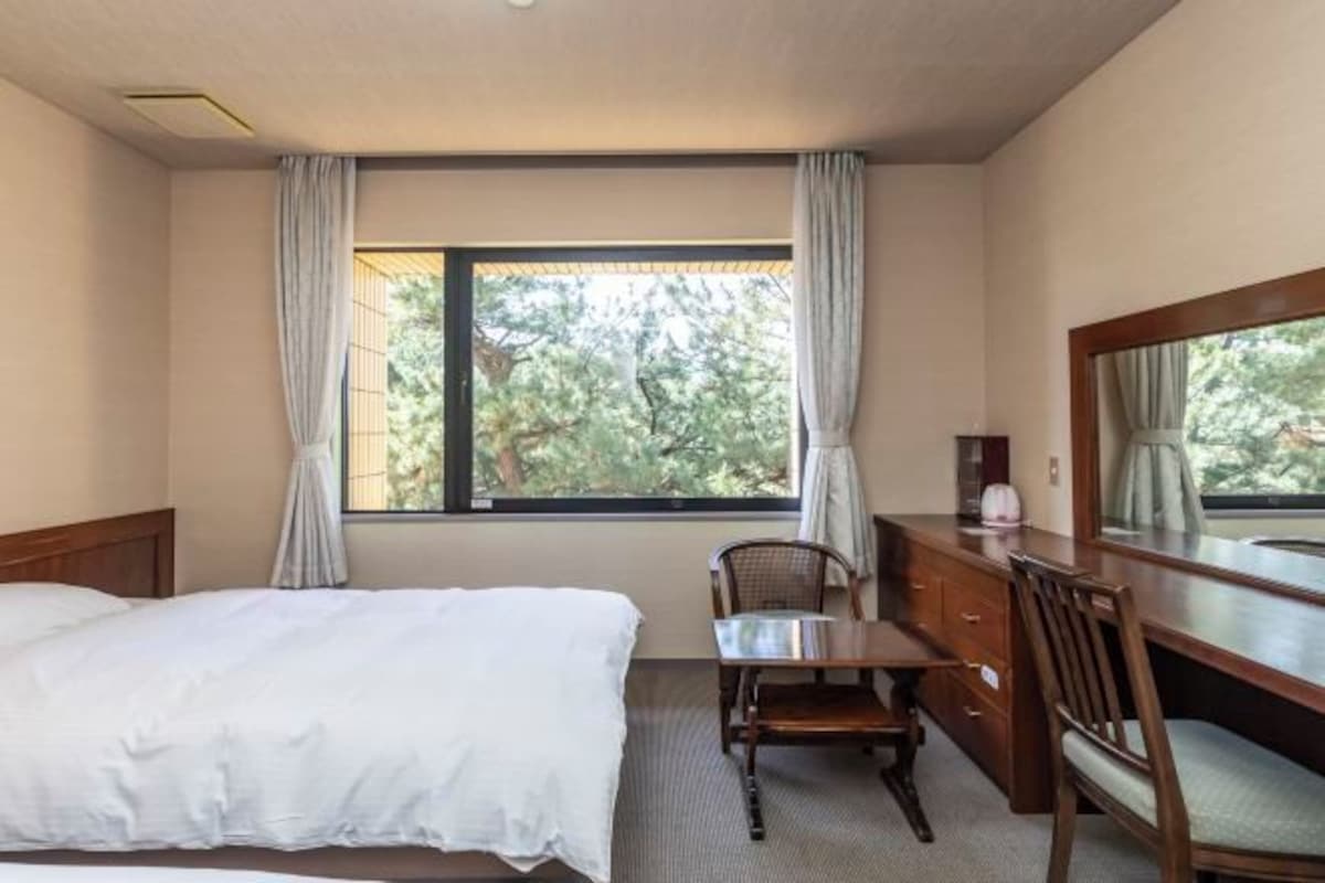A hotel room with a bed, a desk, a chair, and a large window with curtains.