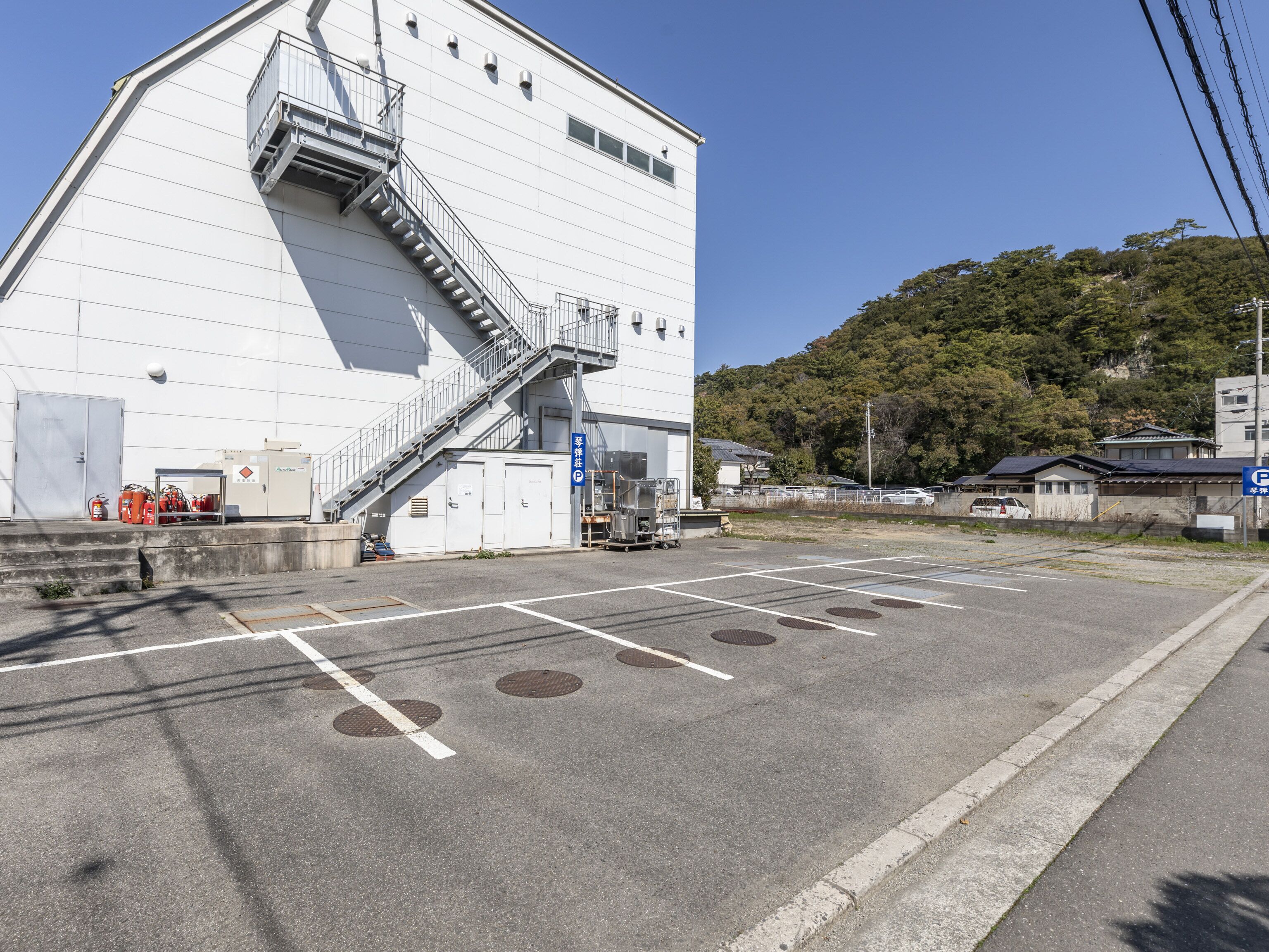 Un grande edificio industriale con una scala che conduce a un piano superiore, un parcheggio con posti delimitati e un cartello che indica un'area di parcheggio.