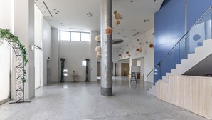 Un vestíbulo espacioso con techo alto, piso de mármol y una columna central. Se observan elementos decorativos en el techo y una escalera a la derecha.
