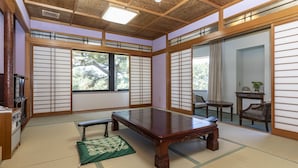 Habitación con esteras de tatami, una mesa de madera baja, puertas correderas y vista a árboles fuera.