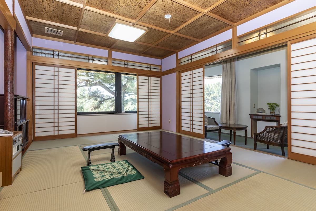 Een kamer met tatami matten, een lage houten tafel, schuifdeuren en uitzicht op bomen.