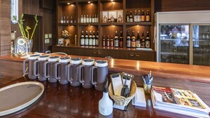 Zona de bar con una barra larga, varias tazas, un reloj y estantes con botellas.
