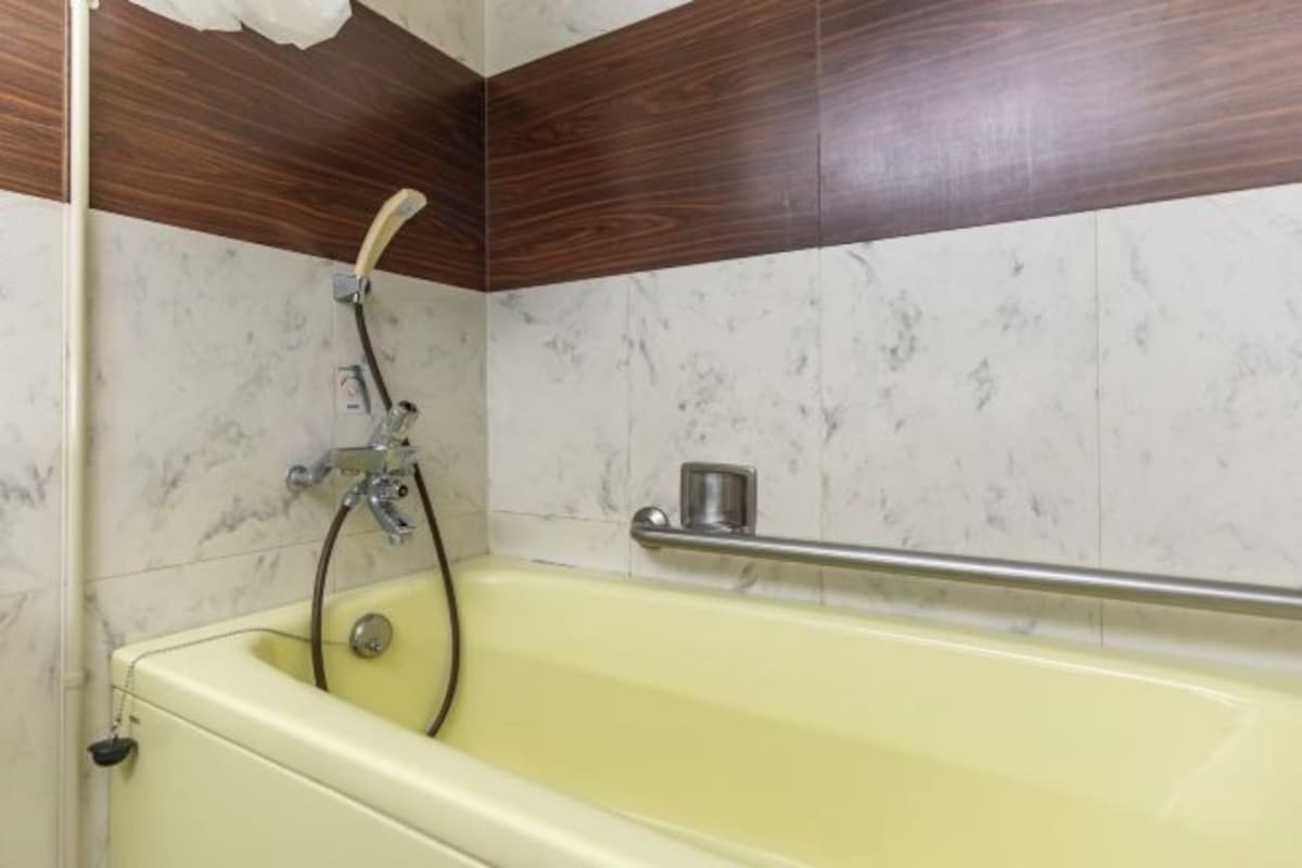A bathroom with a yellow bathtub, a shower, and a marble wall.