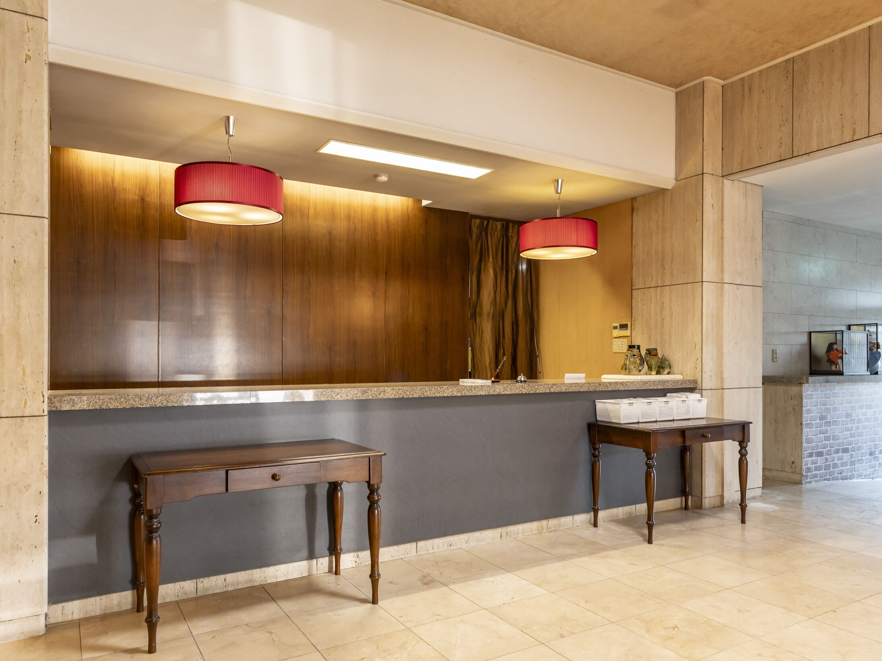 A reception area with a wooden counter, two wooden side tables, a mirror, and pendant lights.
