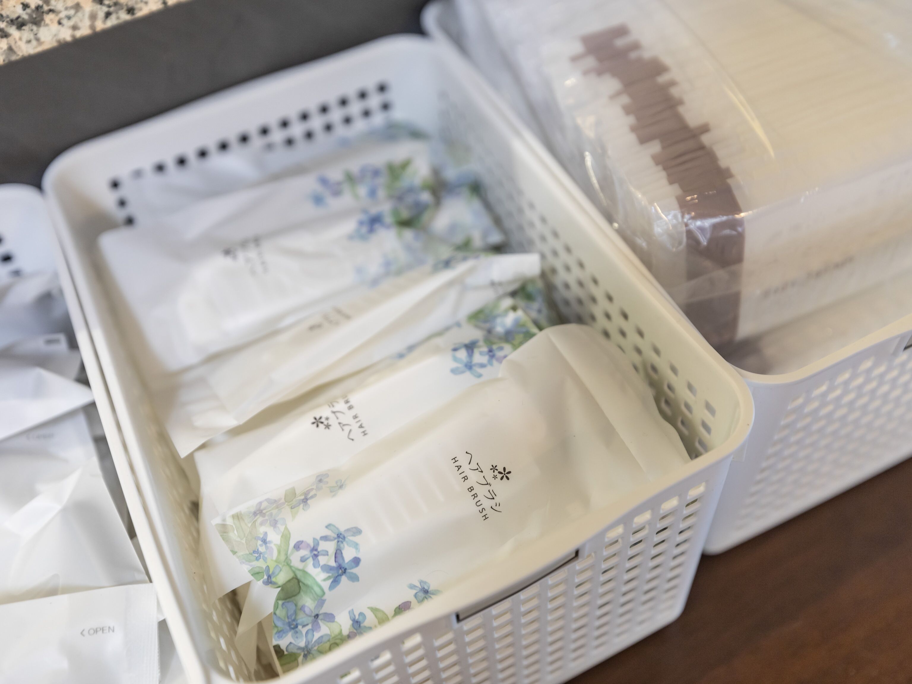 A storage area with white baskets containing folded items, some with floral patterns and text, and a plastic-wrapped item in the background.
