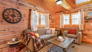 Ein gemütliches Blockhaus-Interieur mit Holzvertäfelung, einer runden Wanduhr, zwei Sofas, einem Couchtisch und einem kleinen Beistelltisch.