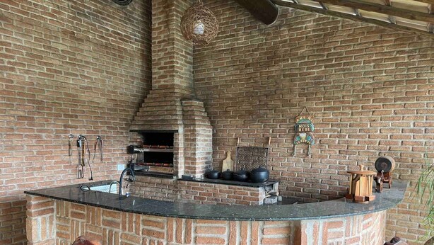 Una cocina rústica al aire libre con pared de ladrillo, un horno de leña y tres taburetes de madera.