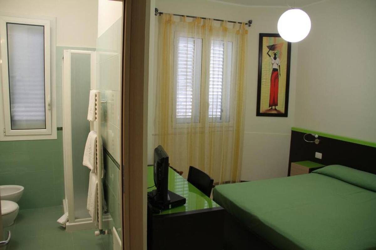 Une chambre d’hôtel équipée d’une douche, de toilettes, d’un lit, d’un bureau avec un ordinateur et d’une fenêtre avec des rideaux.
