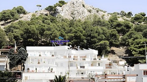 Un hôtel situé sur la côte, avec des bâtiments blancs, une colline rocheuse en arrière-plan et un panneau indiquant la présence d’un restaurant.