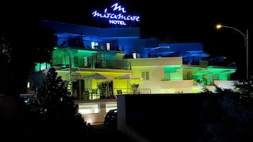 Un hotel a più piani con insegna al neon, area salotto esterna e piscina.