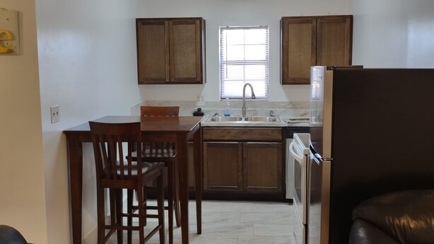 A compact kitchen with wooden cabinets, a dining table with chairs, a refrigerator, and a window with blinds. - Horse Ranch House 2 miles to Austin,  Remodeled, Relaxed Atmosphere, SXSW Near (Manchaca)