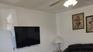 A living room with a flat-screen TV, a glass coffee table, a black leather sofa, a ceiling fan, and two framed pictures on the wall. - Horse Ranch House 2 miles to Austin,  Remodeled, Relaxed Atmosphere, SXSW Near (Manchaca)