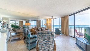 A spacious living room with a large window overlooking the ocean, a comfortable seating area, and a television on a stand.