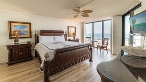 A spacious bedroom with a large bed, a ceiling fan, a view of the ocean, and a dining area with a table and chairs. - Beach Days Beachfront-Edgewater Resort in PCB 2nd Floor-3/3-Amazing! (Panama City Beach)