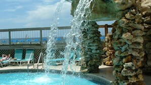 A pool with a waterfall feature, surrounded by lounge chairs and a stone wall. - Beach Days Beachfront-Edgewater Resort in PCB 2nd Floor-3/3-Amazing! (Panama City Beach)