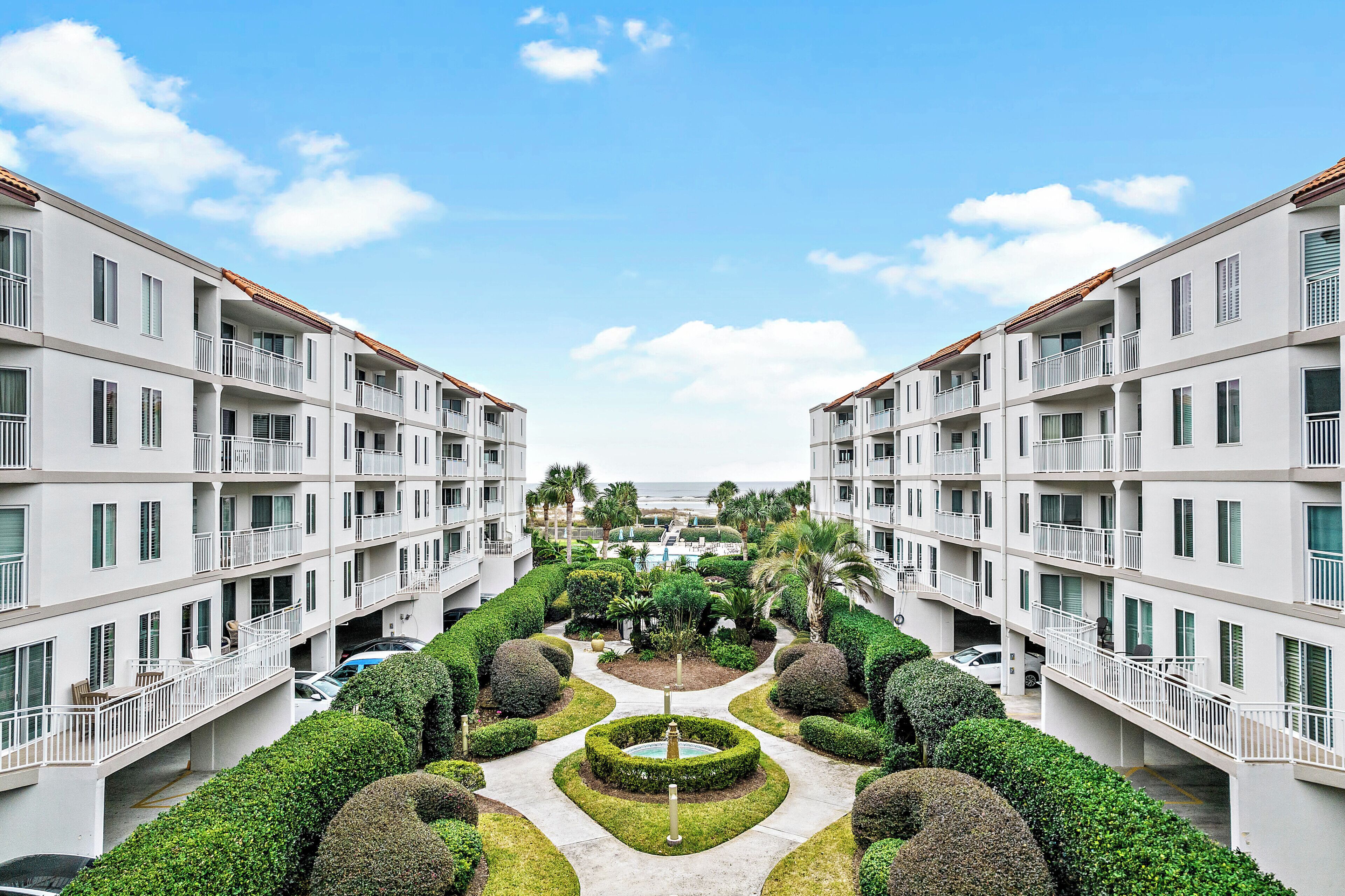 A multi-story hotel with balconies, a central courtyard with hedges, and a view of the ocean.