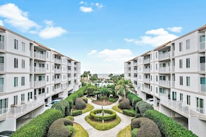 A multi-story hotel with balconies, a central courtyard with hedges, and a view of the ocean.
