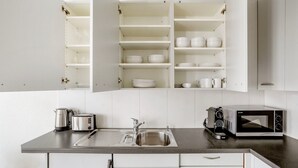 A modern kitchen with white cabinets, a stainless steel sink, a kettle, a toaster, and a microwave. - Stellar Matthäus 1BR w/ Laundry, 13 min to City Center, by Blueground (Basel)