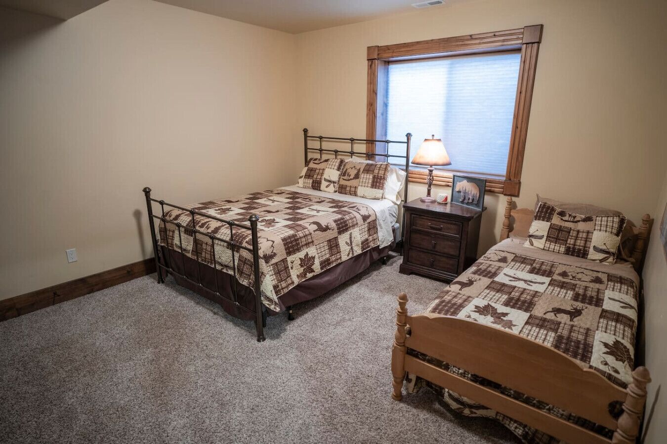 A bedroom with two beds, a nightstand, a lamp, and a window with blinds.