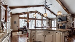 A spacious kitchen with a large island, wooden beams, and a stone fireplace. - New! Moose Manor | Private Boat Dock (Island Park)