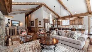 A spacious living room with a high ceiling, rustic wooden beams, a fireplace, and a cozy seating area with a coffee table. - New! Moose Manor | Private Boat Dock (Island Park)