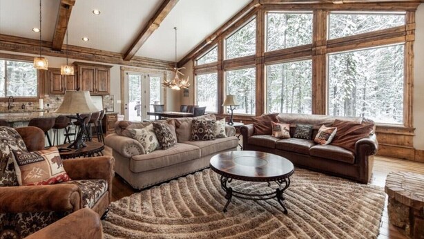 A spacious living room with a large window, a fireplace, and a dining area with a chandelier. - New! Moose Manor | Private Boat Dock (Island Park)